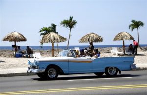 Un grupo de personas disfruta de una playa artificial mientras un auto pasa por el malecón el jueves 21 de mayo de  2015 en La Habana, Cuba. La playa fue creada como parte de la muestra “Detrás del Muro” de la Bienal de Arte de La Habana. (Foto AP/Desmond Boylan)
