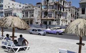 Un grupo de personas disfruta de una playa artificial mientras un auto convertible clásico lleva a unos novios por el malecón de La Habana, el jueves 21 de mayo de 2015 en La Habana, Cuba. La playa fue creada como parte de la muestra “Detrás del Muro” de la Bienal de Arte de La Habana.  (Foto AP/Desmond Boylan)
