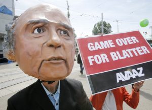A protester wearing a mask depicting FIFA President Sepp Blatter stands in front of the building where the 65th FIFA congress takes place in Zurich, Switzerland, Friday, May 29, 2015. Protesters from the global campaign movement Avaaz demand the resignation of  Blatter over the FIFA corruption scandal and rights abuses of World Cup construction workers in Qatar. (AP Photo/Michael Probst