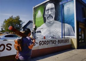 Un hombre, guitarra al hombro, pasa frente a una imagen del actor Danny Trejo pintada por el muralista Levi Ponce. Foto: AP