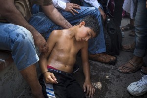 Un niño sirio, sufriendo de los estragos del golpe de calor, se sienta bajo el cuidado de migrantes y refugiados que esperaban entrar a Grecia. Foto: AP
