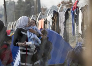 Una madre migrante sostiene a su bebé en brazos mientras esperan en el lago griego de la frontera entre Grecia y Macedonia para cruzar al país, el 1 de marzo de 2016. (Foto AP/Visar Kryeziu)